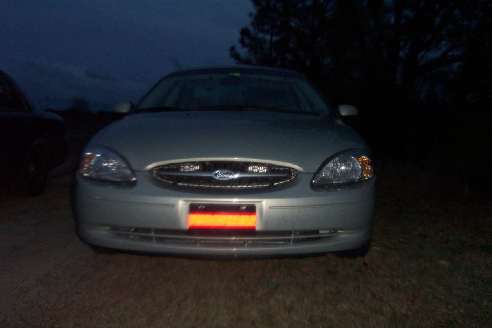 Front view of a silver 2003 Ford Taurus parked at night. Another dark vehicle is partially visible on the left