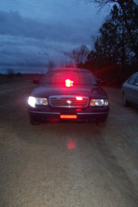 1998 Ford Crown Victoria - A 1998 Ford Crown Victoria police car is seen from the front at dusk, with its emergency lights activated.