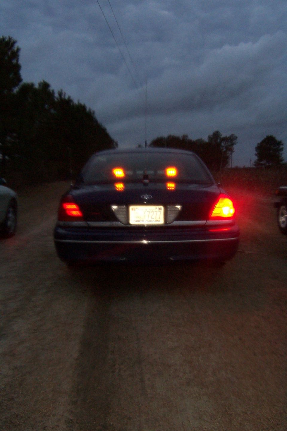 Dark blue 1998 Ford Crown Victoria with rear lights illuminated, parked on a dirt road