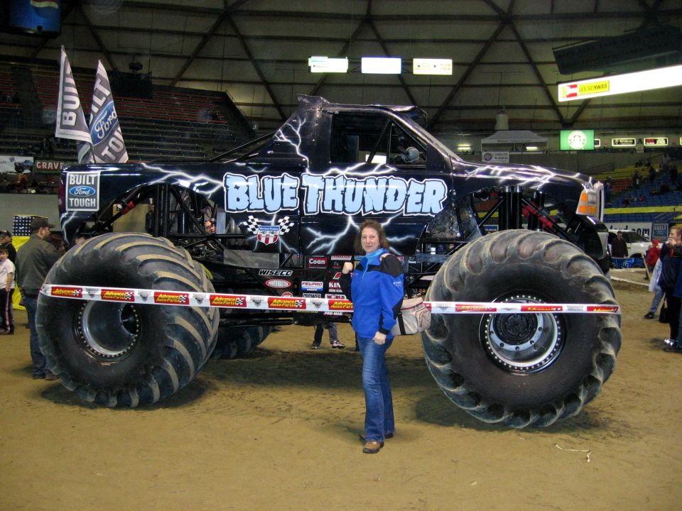 Black monster truck with lightning graphics and 'Blue Thunder' text, a woman stands in front