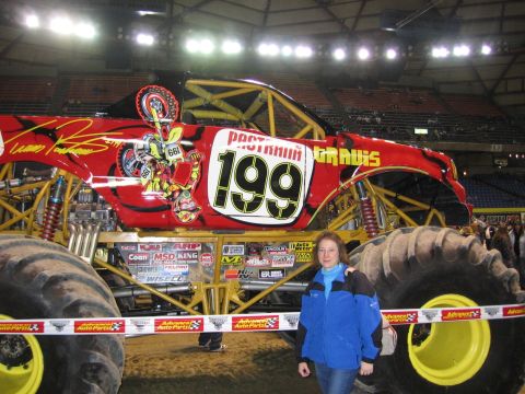 1976 Ford F-150 - A woman poses next to a monster truck with the number 199 displayed prominently on its side.
