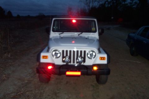 2006 Jeep Wrangler - A white 2006 Jeep Wrangler is seen from the front at dusk, illuminated by its red emergency lights.