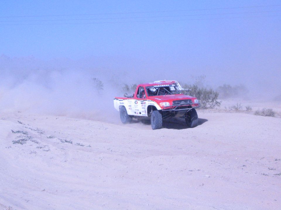 Red and white off-road race truck cornering on desert sand