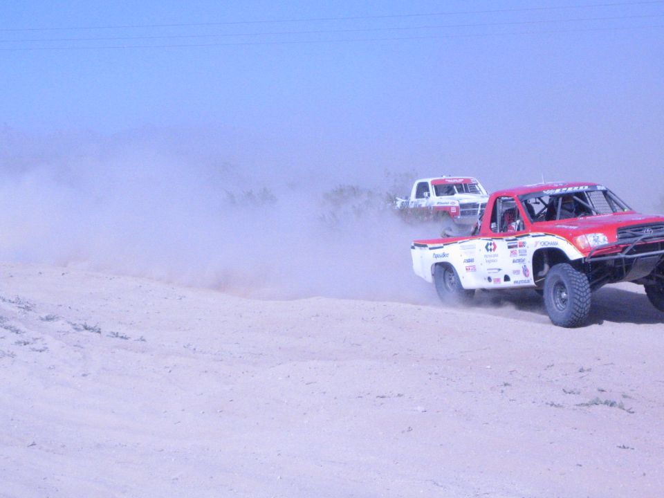 Two off-road race trucks on a dusty desert course