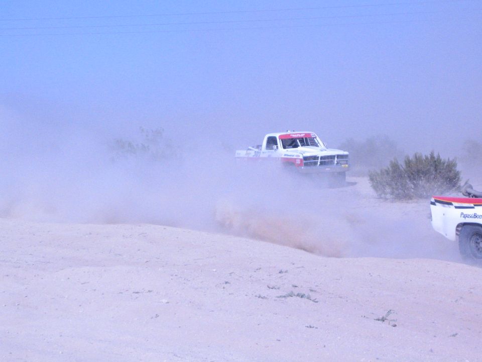White race truck and trailing truck in heavy desert dust