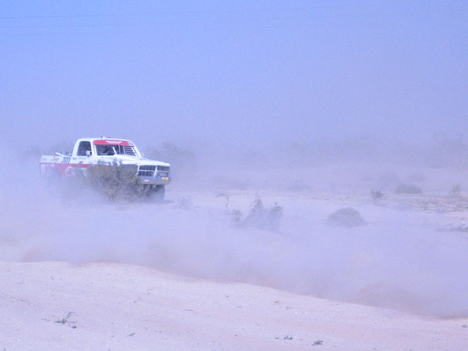 White and red race truck driving through desert dust haze