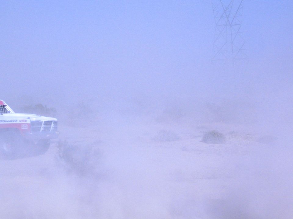 Race truck partly hidden in heavy desert dust cloud