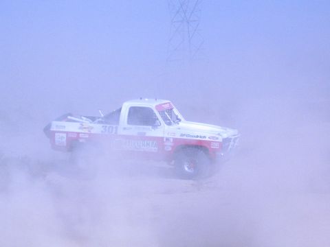 1990 Ford Bronco - Off-road race truck number 301 with sponsor graphics drives through a dense desert dust cloud.