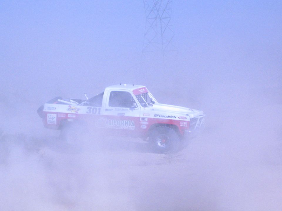 Red and white race truck number 301 in desert dust