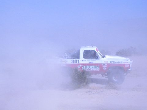 1990 Ford Bronco - Off-road race truck number 301 sprays sand and dust as it powers across the open desert.