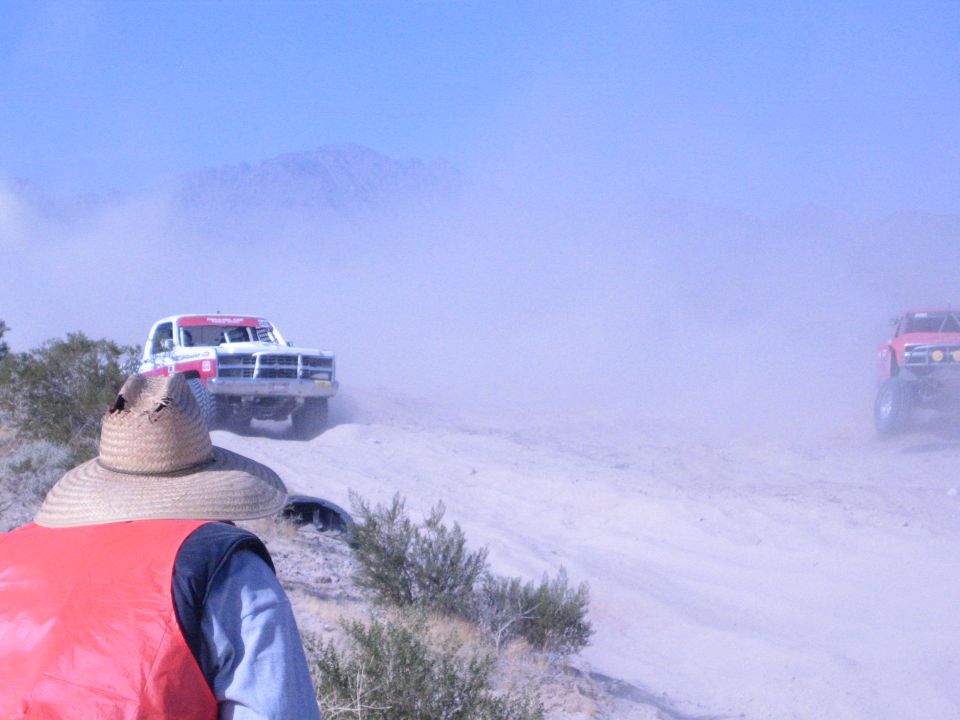 Two race trucks approaching a spectator across the desert