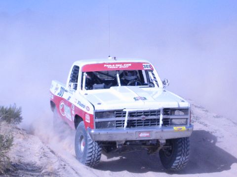 1990 Ford Bronco - white-and-red off-road race truck numbered 301, lettered Phils Inc.com, charges through a dusty desert course.