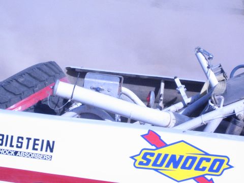 1990 Ford Bronco - Detail of a race truck's open rear bed revealing tubular chassis, hardware, and Bilstein and Sunoco decals on the side panel.