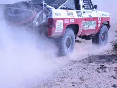 1990 Ford Bronco - Three-quarter rear view of California Tow race truck 301 trailing a plume of dust on a desert course.