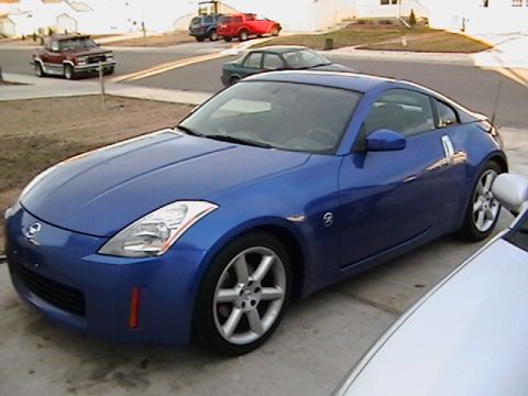 2003 Nissan 350Z - A blue 2003 Nissan 350Z is parked in a driveway with other vehicles visible in the background.