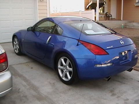 2003 Nissan 350Z - A blue 2003 Nissan 350Z coupe is parked in front of a garage, showing its rear and side profile.