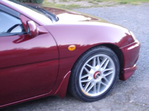 1993 Mazda MX-3 - Close-up of the front passenger side of a red coupe, showing the wheel and fender.