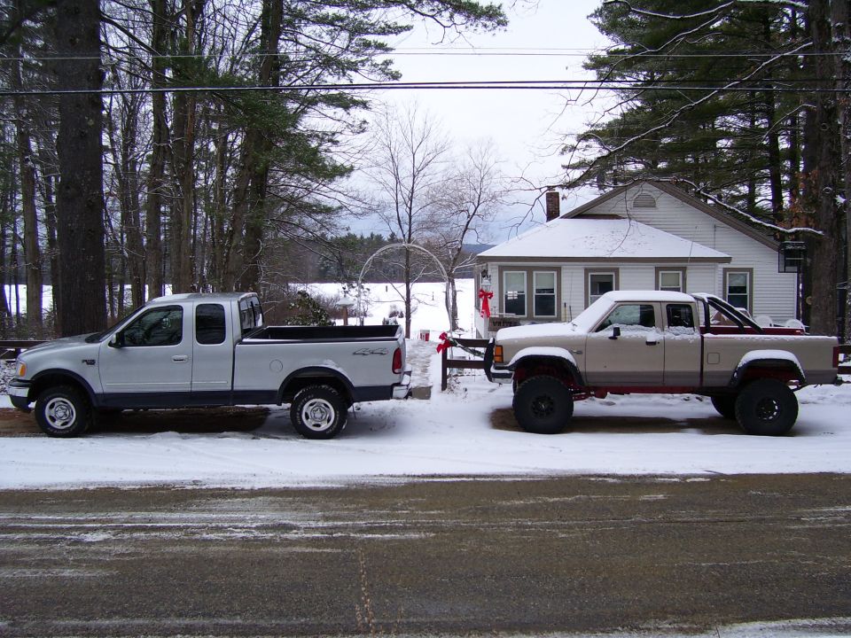 Lifted red and tan Ford Ranger pickup facing a silver F-150 on a snowy street in front of a white house