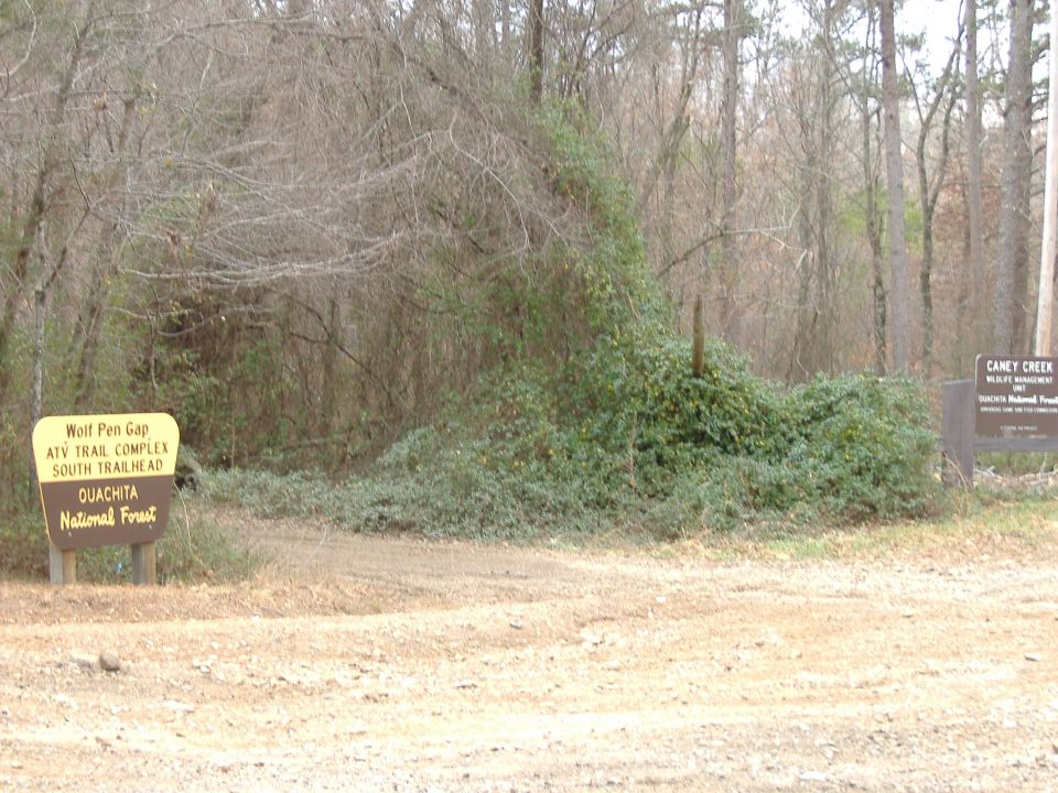 Yellow and brown trailhead signs in a wooded area with dry brush