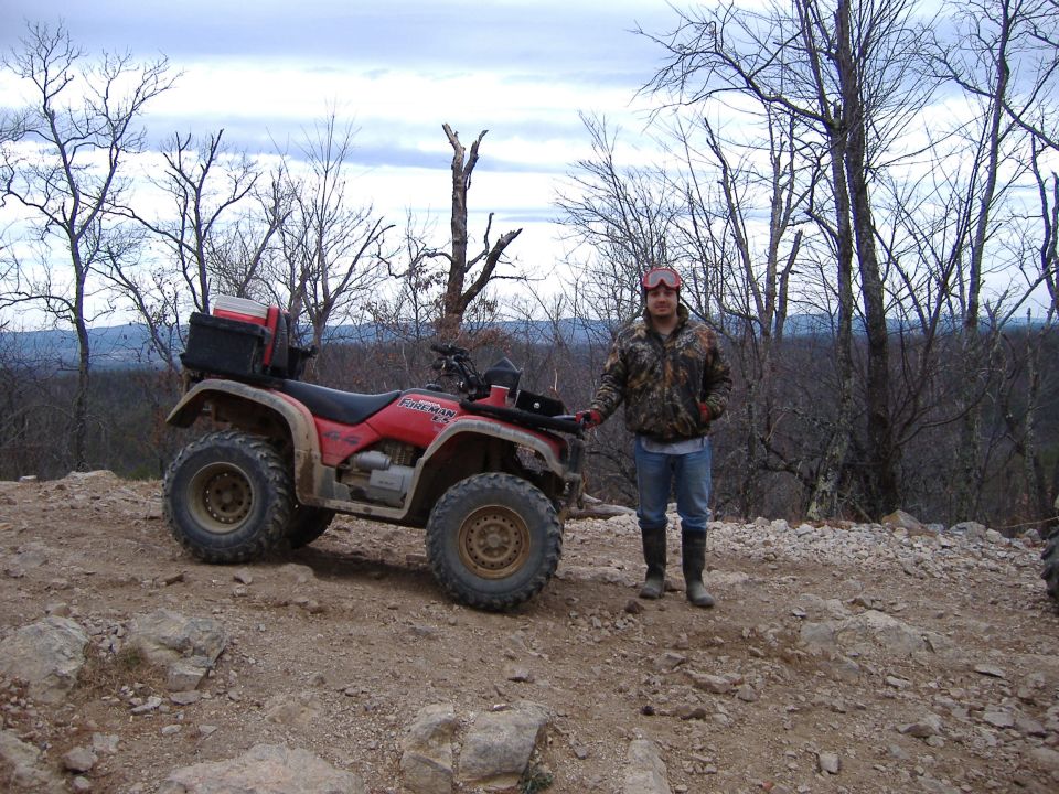 Red Honda Foreman 4x4 ATV on rocky ridge trail with rider standing beside it