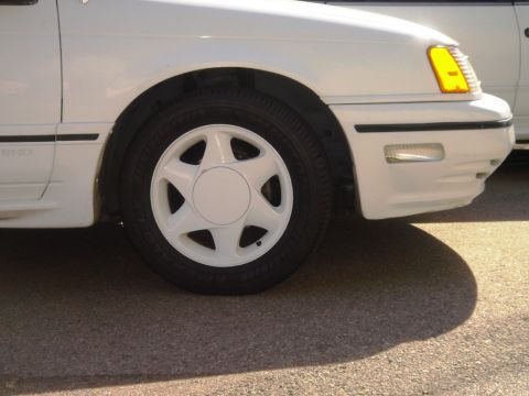 1991 Ford Taurus - A white 1991 Ford Taurus is partially visible from the front quarter, revealing its distinctive wheel and front fender.