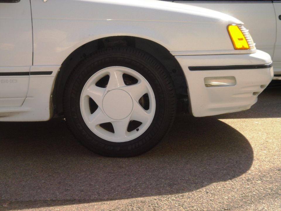 White 1991 Ford Taurus front fender and wheel, showing a white star-spoke wheel and yellow turn signal