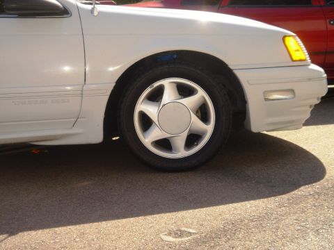 1991 Ford Taurus - Close-up of a white sedan's front fender and wheel, showing the 'TAURUS SHO' badging.