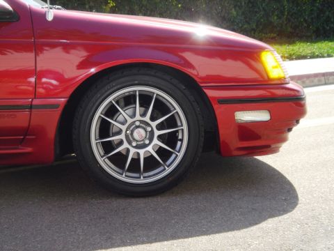 1991 Ford Taurus - Close-up of a red 1991 Ford Taurus showing the front fender and wheel with aftermarket BBS rims.