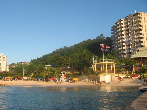 1991 Ford Bronco - A tropical beach scene with a large hotel and lush green hills in the background.