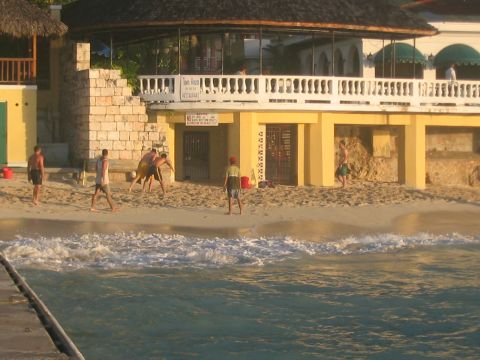 1991 Ford Bronco - A group of people engage in a game of volleyball on a tropical beach, with a building and ocean in the background.