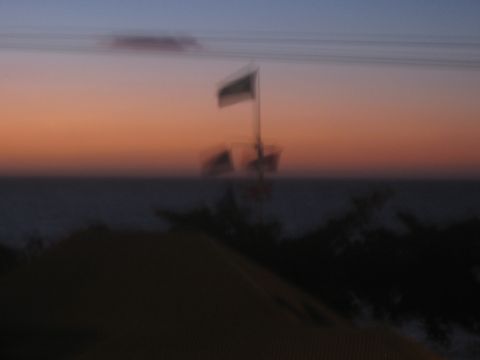 1991 Ford Bronco - A boat with a flag sails on the water as the sun sets, casting an orange glow across the sky.