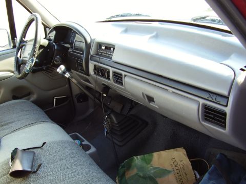 1996 Ford F-150 - Interior view of a Ford pickup from the driver's side, showing the gray dashboard with 'XL' trim badge, a manual shifter, aftermarket black…