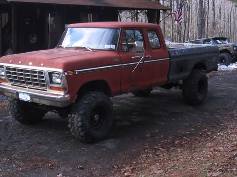 1979 Ford Bronco - A red 1979 Ford F-150 pickup truck with a black bed and lifted suspension is parked outside a cabin.