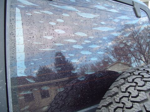 1989 Jeep YJ - Water droplets and streaks are visible on the rear window of a vehicle, with a spare tire mounted nearby.