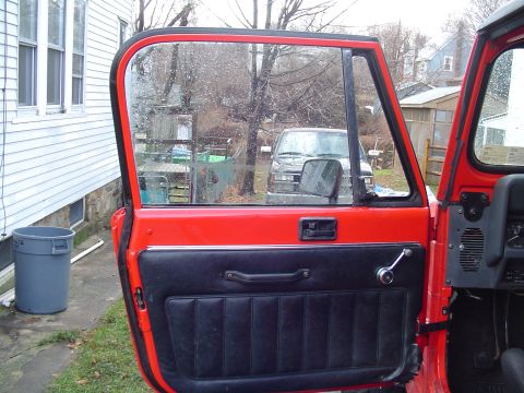 1989 Jeep YJ - Red Jeep YJ door open, revealing black interior and a glimpse of another vehicle outside.