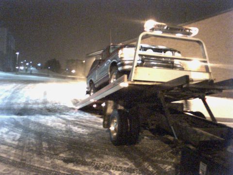 1995 Ford Bronco - A tow truck transports a vehicle on its flatbed during a snowy night.