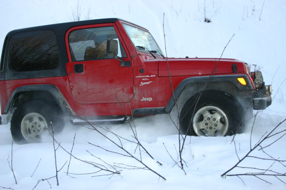 Red Jeep Wrangler driving through snow, kicking up dust
