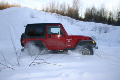 2003 Jeep TJ - A red Jeep Wrangler navigates a snowy terrain, its tires churning up snow.