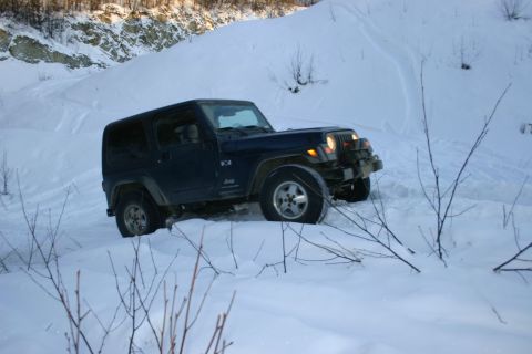 2003 Jeep TJ - A Jeep TJ navigates a snowy, off-road path with steep, snow-covered hills in the background.