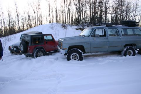 2003 Jeep TJ - A red Jeep TJ and two other SUVs are stuck in a snowy landscape with trees in the background.