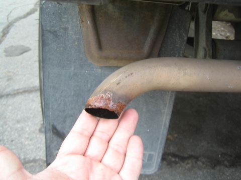 1987 Suzuki Samurai - Close-up of a rusty exhaust pipe end held by a hand, with a mud flap visible in the background.
