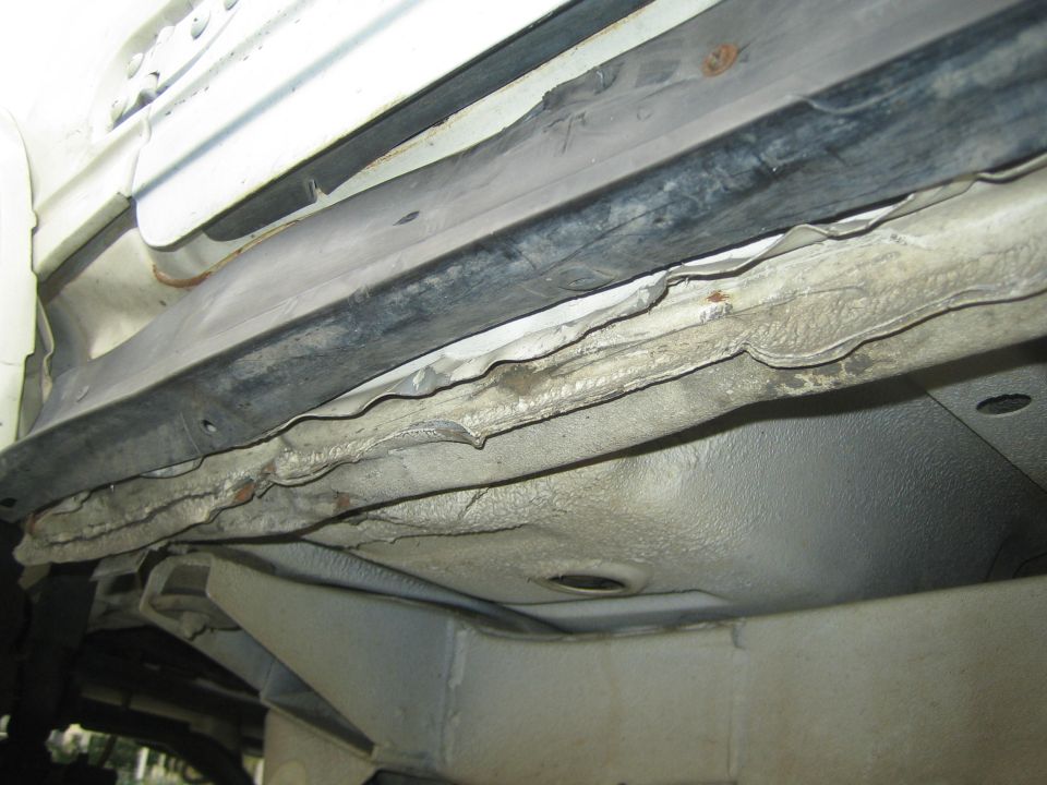 Undercarriage of a vehicle showing rusted rocker panel and frame