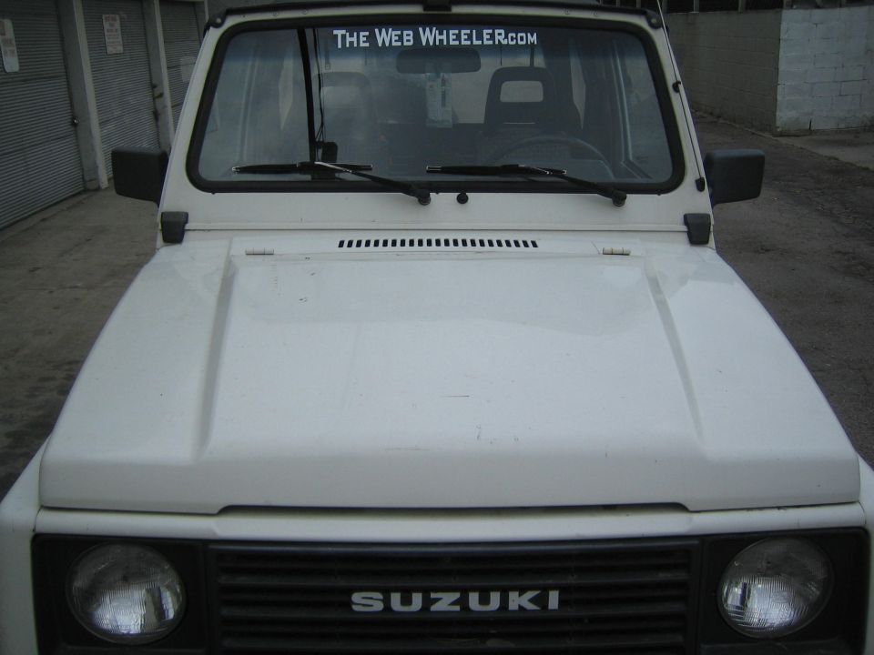 White 1987 Suzuki Samurai front view with "THE WEB WHEELER.COM" sticker on windshield