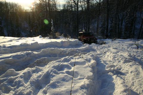 2003 Jeep TJ - A red Jeep navigates a snowy path, leaving tracks in the deep snow.