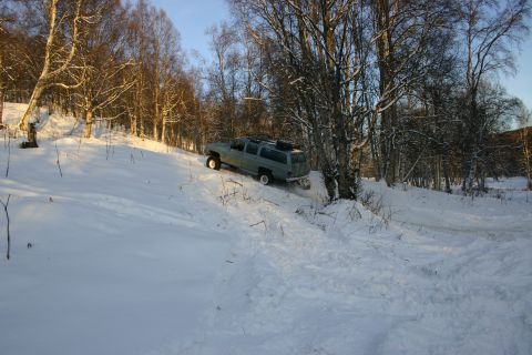 2003 Jeep TJ - A gray SUV navigates a snow-covered slope amidst a wooded area.