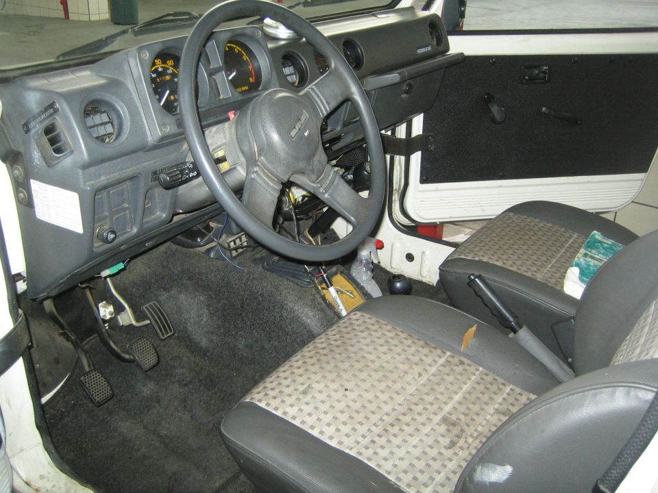 Interior of a 1987 Suzuki Samurai showing the dashboard, steering wheel, seats, and floor pedals