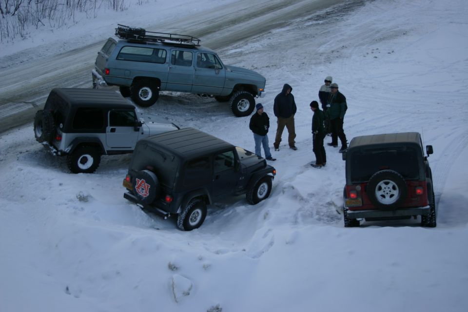 Four Jeeps and a large SUV parked in snow, with people standing around