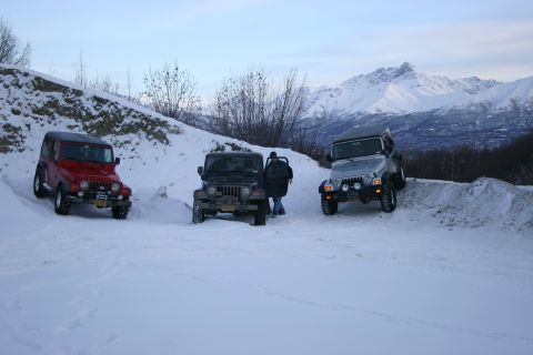 2003 Jeep TJ - Three Jeep Wranglers navigate a snow-covered trail with a mountainous backdrop.
