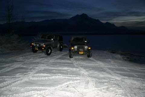 2003 Jeep TJ - Two Jeep TJs sit in a snowy landscape as dusk settles, with mountains visible in the distance.