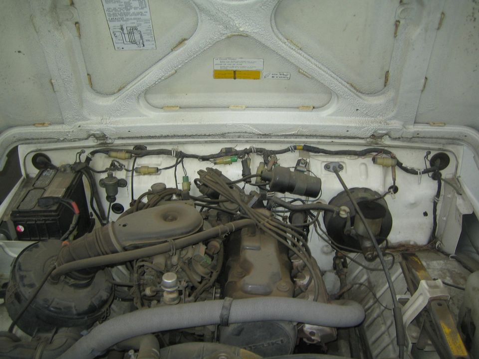 1987 Suzuki Samurai engine bay with a V6 engine, battery on the left, and various hoses and wires